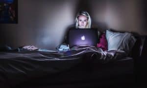 A woman sitting on her laptop from bed in the dark