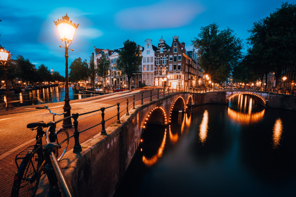 Night city view of Famous Keizersgracht Emperor's canal in Amsterdam, tranquil scene with a street lantern, an illuminated bridge at twilight, Netherlands.