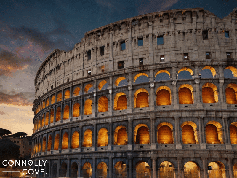 The Colosseum of ancient Rome at dusk, illuminated from within against a partly cloudy sky. "Connolly Cove" text is visible in the lower left corner.