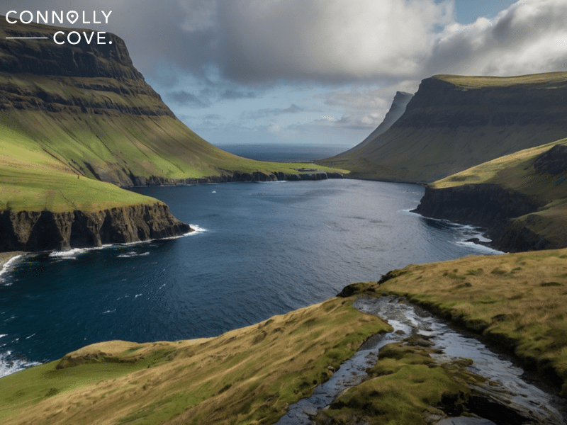 faroe islands 
A rugged coastline with steep green cliffs reminiscent of the Faroe Islands surrounds a deep blue bay under a partly cloudy sky; "Connolly Cove" text in the top left corner.