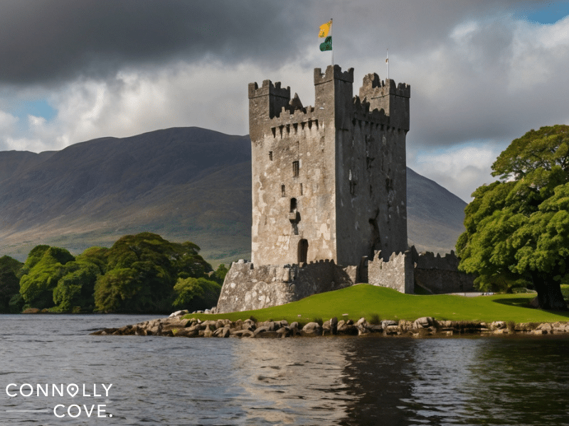 Ross Castle, with its battlements, stands on a grassy island by a lake, framed by mountains and trees. Two flags fly atop the tower.