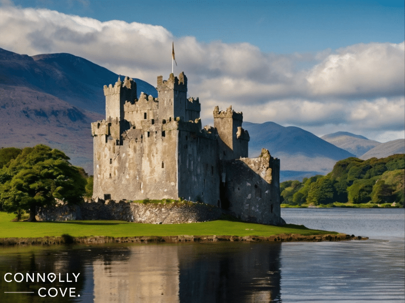 Ross Castle sits on a small grassy island surrounded by water, with mountains and trees in the background under a partly cloudy sky.