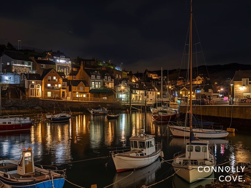 Mousehole Cornwall harbour with famous Christmas lights reflecting on water at night