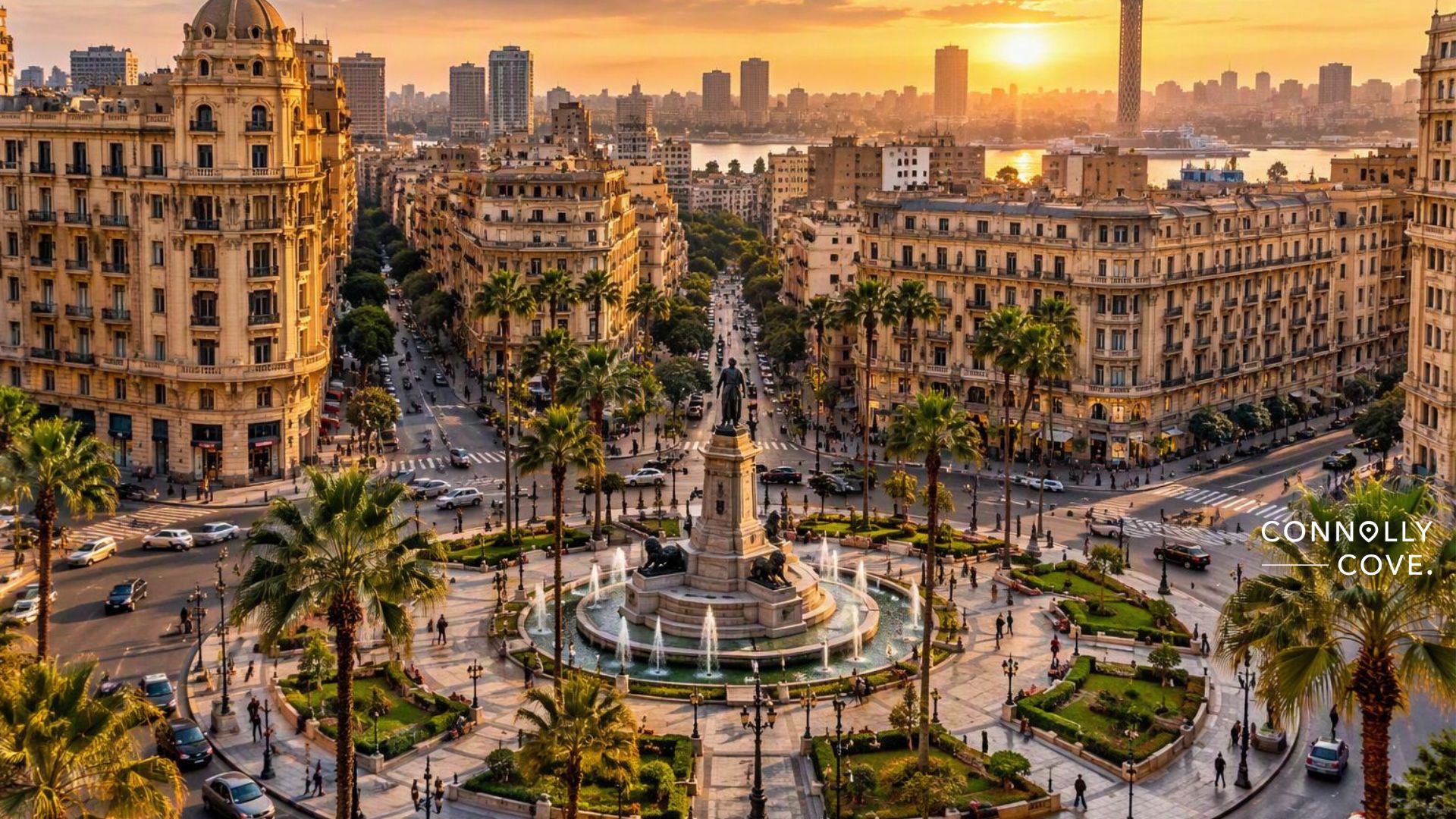 A sunset view of a busy city centre square of downtown Cairo with a central fountain, surrounded by historic buildings, palm trees, and busy streets. The river and skyline are visible in the background.