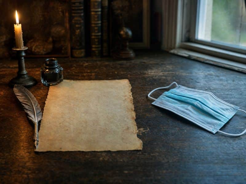 Quill, blank parchment and a modern face mask on an oak desk, showing how pandemics influence culture across the centuries