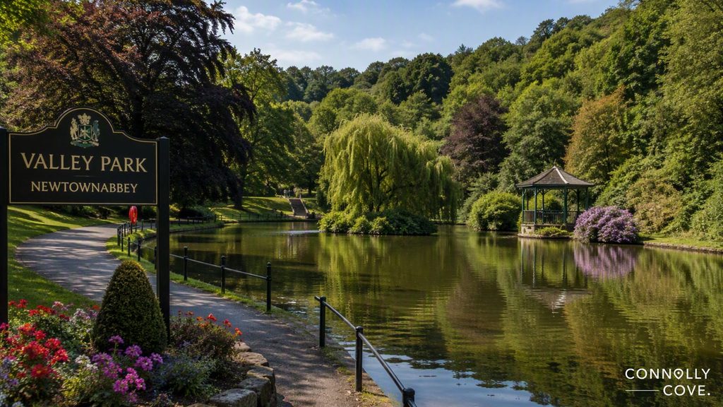 A serene park scene with a pond, lush greenery, a gazebo, and a Valley Park Newtownabbey sign. Trees and flowers surround the calm water under a clear sky, capturing the natural beauty of County Antrim’s beloved Valley Park in Newtownabbey.