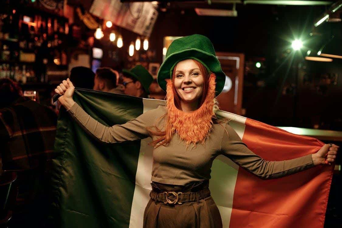 A woman dressed as a leprechaun and holding an Irish flag