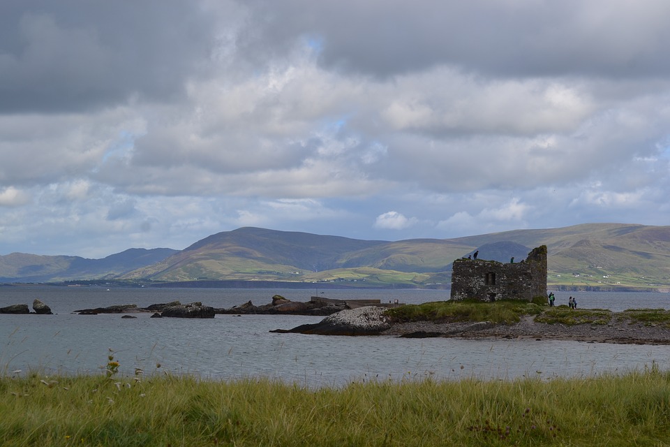 A stone ruin sits on a small, grassy island near the shore—capturing the timeless charm that makes Ireland one of the best cities to visit in Ireland, with calm water and distant hills under a cloudy sky in the background.