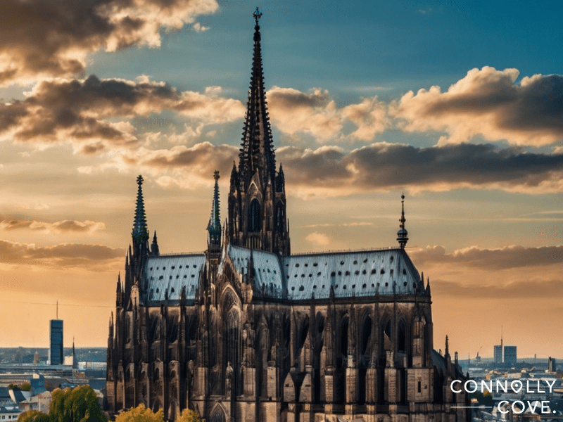 koeln 
A Gothic-style cathedral with tall spires stands against a sunset sky in Cologne, city buildings visible in the background. The text "CONNOLLY COVE" appears in the lower right corner.