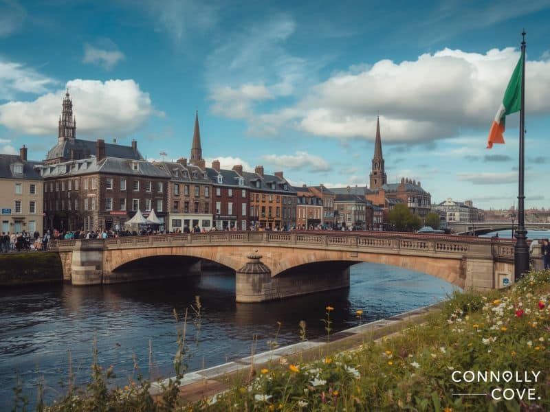 A stone bridge crosses a river in a European city with historic buildings and church steeples in the background. People walk along the bridge near an Irish flag, evoking the lively spirit of Temple Bar on a classic Dublin holiday under a partly cloudy sky.