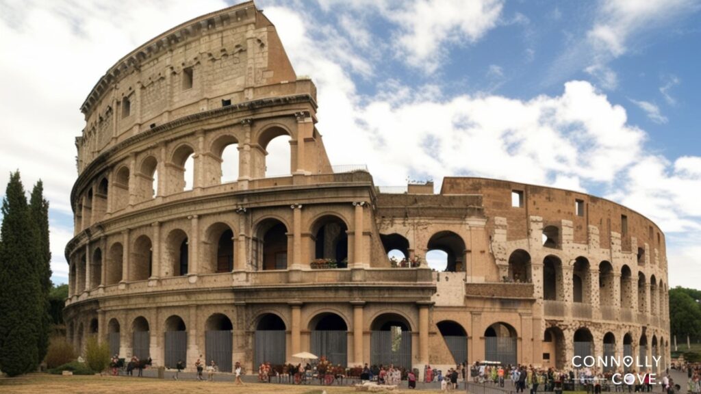 The Colosseum in Rome, Italy, stands against a partly cloudy sky with many tourists—including Italians enjoying domestic tourism—gathered around its base. The ancient amphitheater’s arched exterior is partially weathered but still impressive.