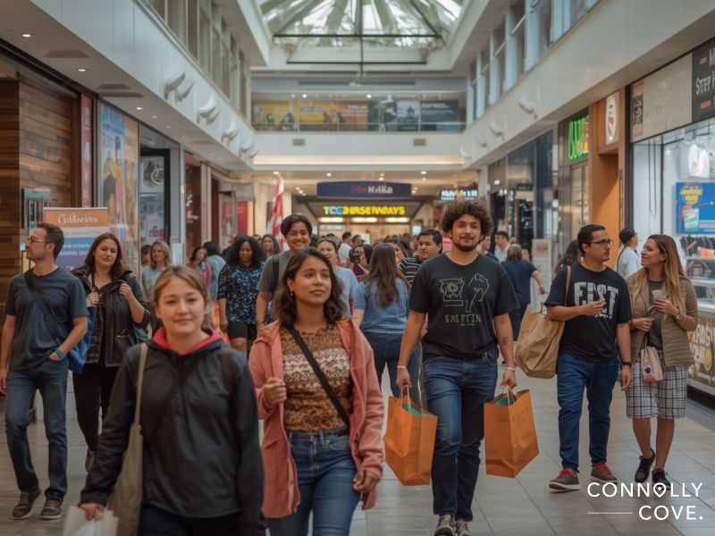 A busy shopping mall like Cairo Festival City Mall with diverse people walking and carrying shopping bags. Storefronts line both sides and a skylight above creates a bright, lively atmosphere.