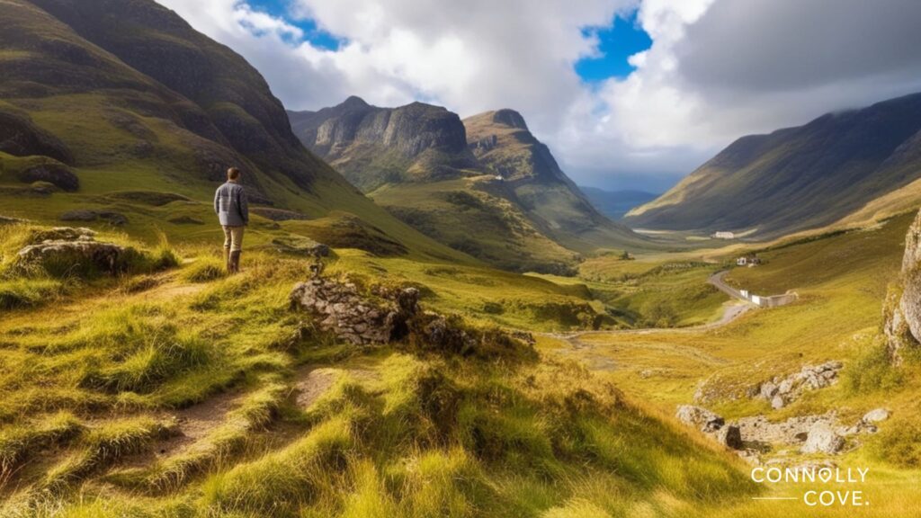 A person stands on a grassy hillside in Scotland, overlooking a vast, green valley surrounded by rugged mountains under a partly cloudy sky. The dramatic landscape hints at iconic Scottish landmarks. Connolly Cove is written in the corner.