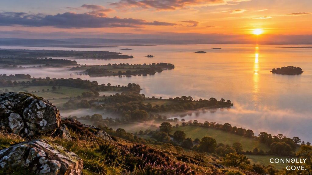 Aerial view of a misty Lough Neagh at sunrise, with small islands and forested shorelines.