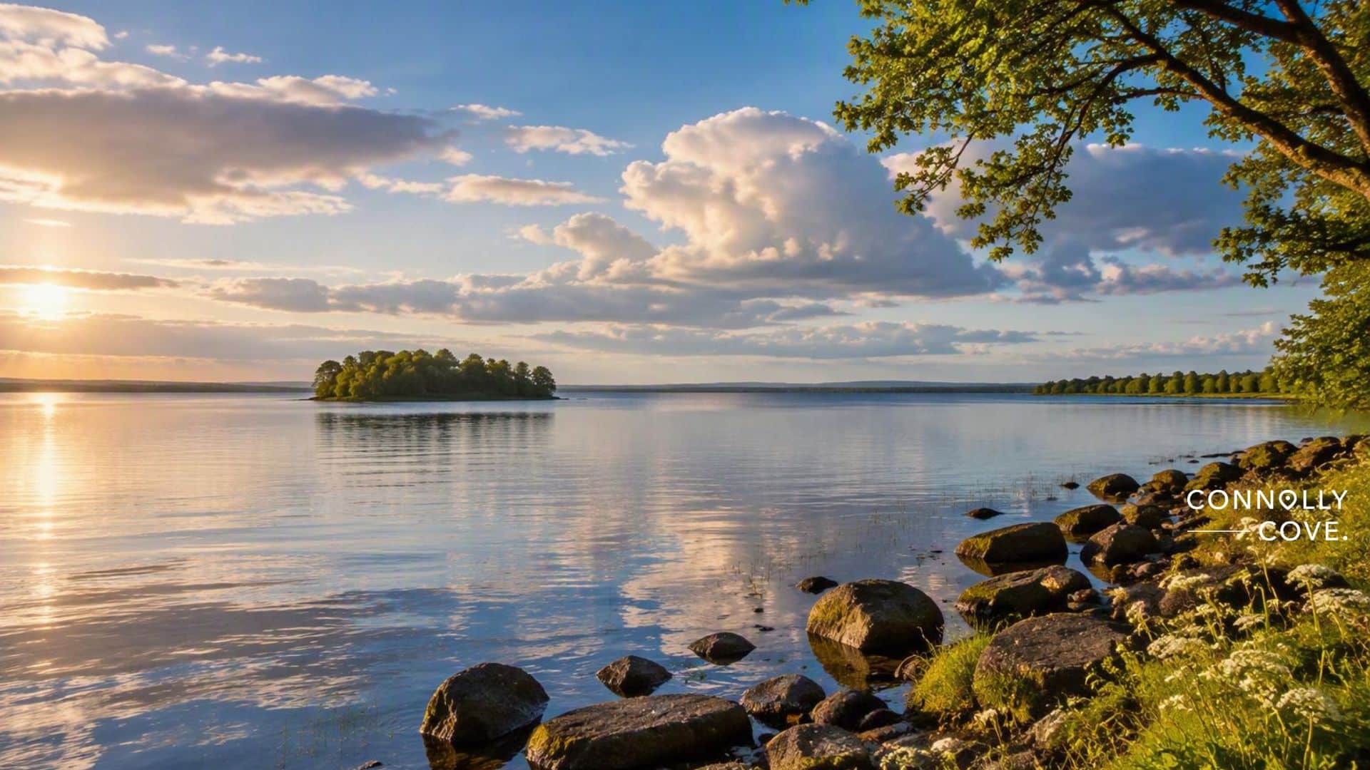 A small, tree-covered island sits in the middle of Lough Neagh during sunset, with rocks lining the calm foreground shore.